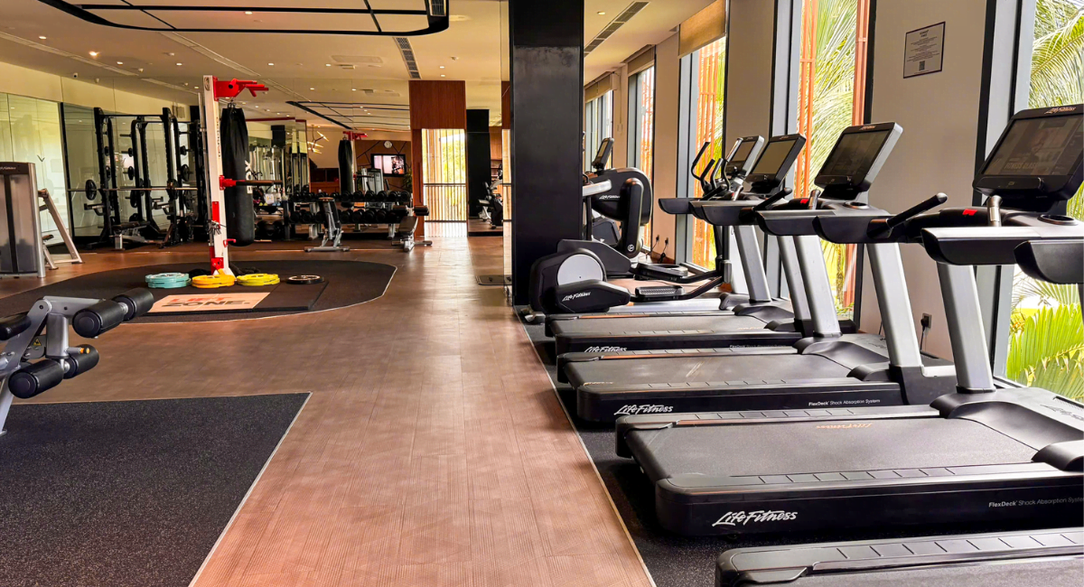 Hàng máy chạy bộ hiện đại đặt cạnh cửa kính lớn trong phòng tập gym của khu resort